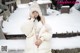 A woman sitting on a bench in the snow wearing a white coat.