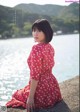 A woman in a red dress sitting on a rock by the water.