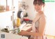 A woman in an apron standing in a kitchen next to a sink.